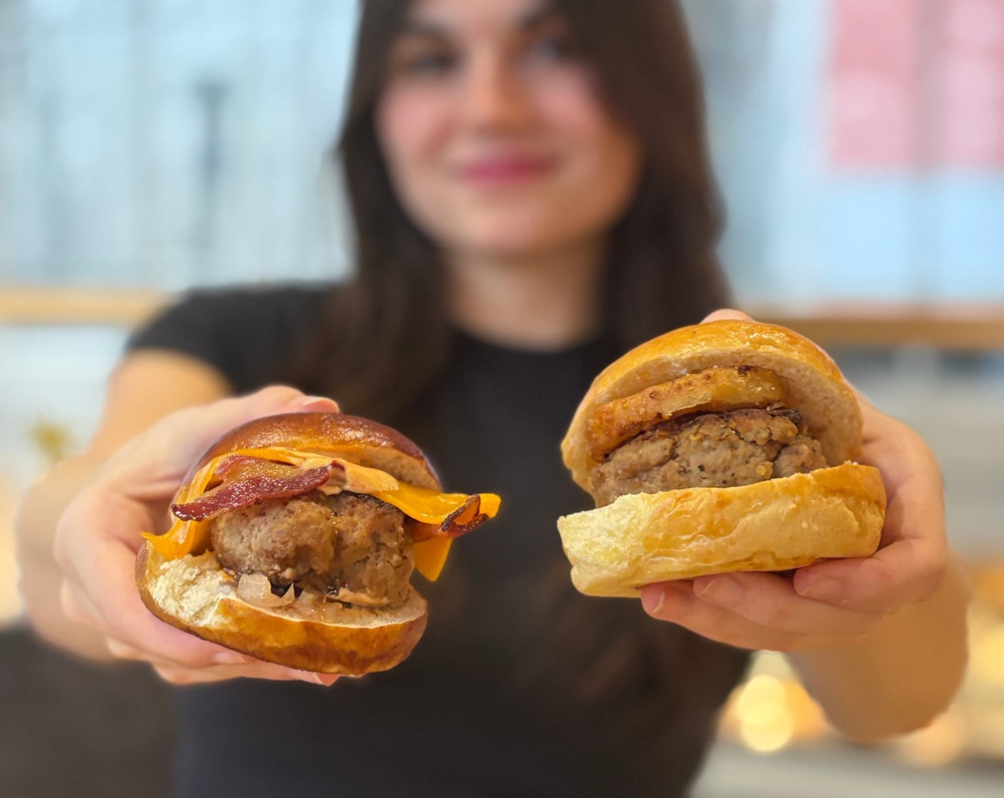 A woman holds up two burgers as part of the Burger Brawl, a residential dining culinary cookoff designed to highlight sustainable, plant-forward burger options and engage students in selecting the winning recipe.